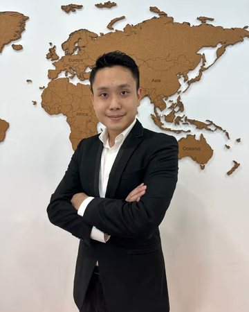 Alan Goh in a dark suit, arms crossed, in front of a world map